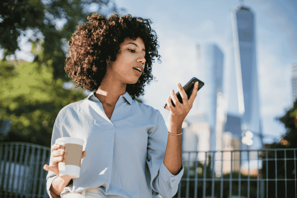 A woman sat in the park with a coffee and talking into her phone
